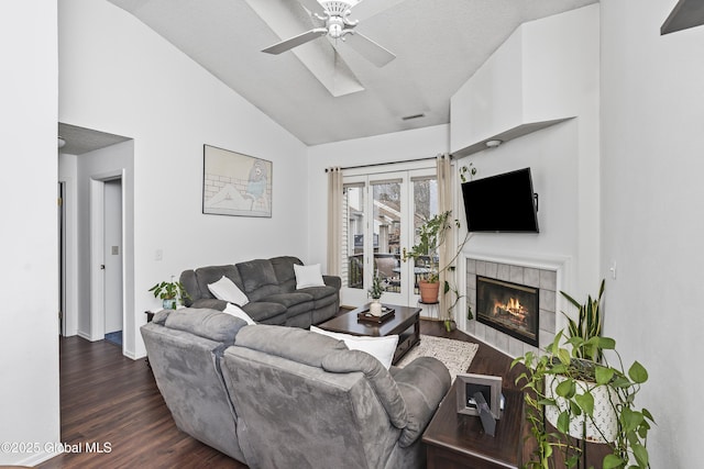 living area featuring visible vents, vaulted ceiling, a tile fireplace, dark wood-style floors, and a ceiling fan