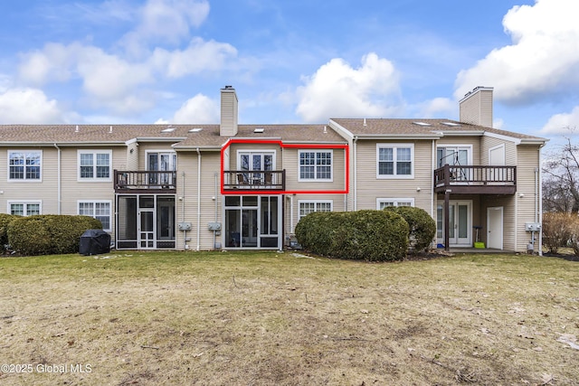 back of property with a balcony, a chimney, a yard, and a sunroom