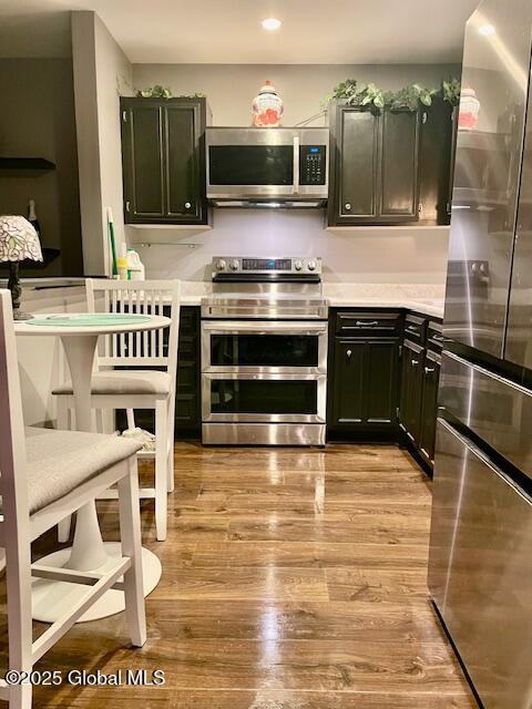 kitchen with dark cabinetry, light wood-style floors, appliances with stainless steel finishes, and light countertops