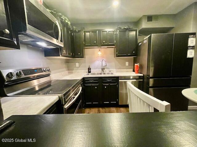 kitchen featuring dark wood-type flooring, a sink, stainless steel appliances, light countertops, and dark cabinets