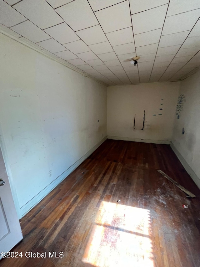 empty room featuring wood-type flooring, baseboards, and a paneled ceiling