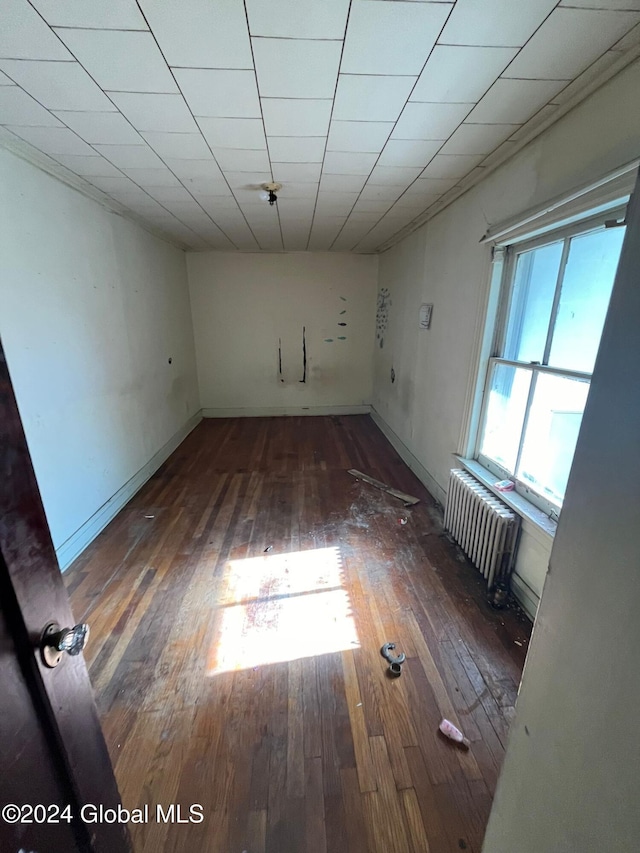 spare room with radiator, a drop ceiling, baseboards, and hardwood / wood-style floors