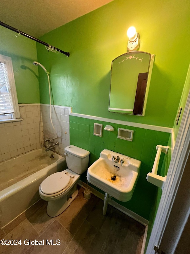 full bath featuring tile walls, toilet, a sink, wainscoting, and shower / bathtub combination