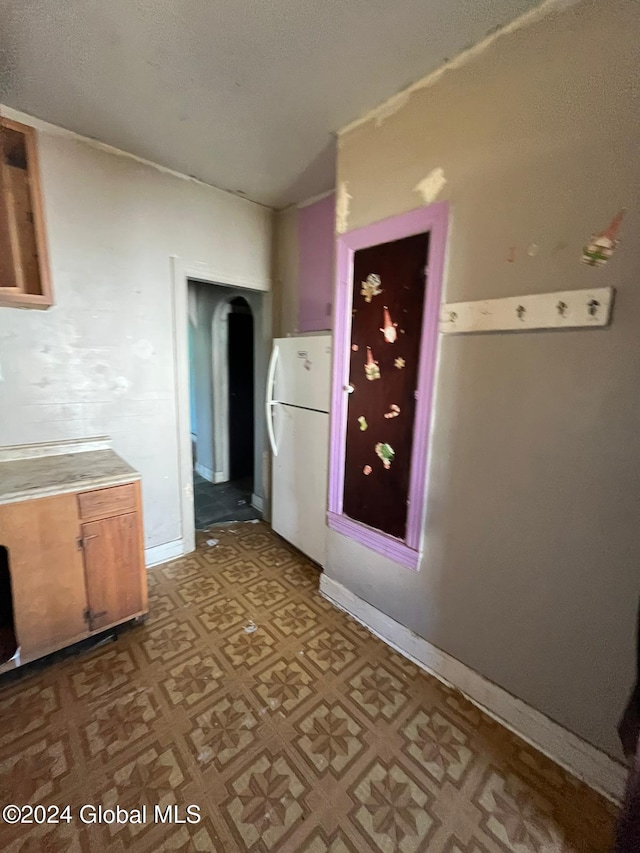 kitchen with tile patterned floors, vaulted ceiling, light countertops, freestanding refrigerator, and baseboards