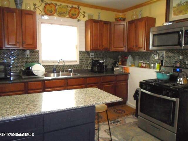 kitchen with ornamental molding, a sink, light stone counters, appliances with stainless steel finishes, and decorative backsplash