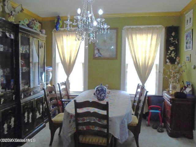 carpeted dining space featuring an inviting chandelier and ornamental molding