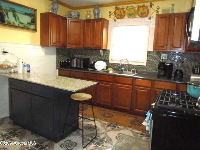 kitchen featuring a breakfast bar, a sink, decorative backsplash, black range with gas cooktop, and crown molding