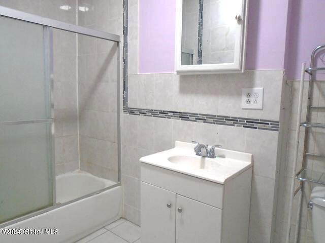 full bathroom featuring tile patterned flooring, vanity, tile walls, and bath / shower combo with glass door