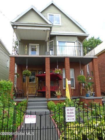 view of front facade featuring a balcony, covered porch, and a fenced front yard