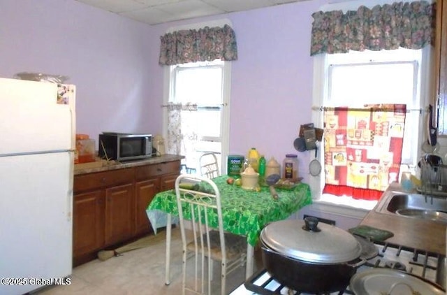 kitchen with stainless steel microwave, brown cabinets, freestanding refrigerator, and a sink