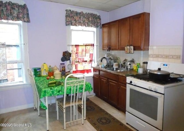 kitchen featuring white range with gas cooktop, brown cabinets, tasteful backsplash, and a sink