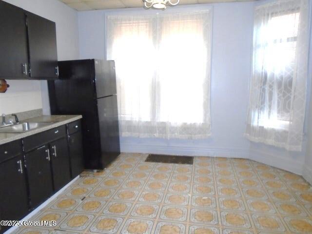 kitchen featuring a sink, dark cabinetry, light countertops, and freestanding refrigerator