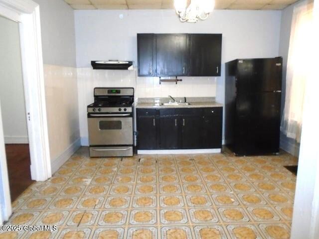 kitchen featuring under cabinet range hood, backsplash, stainless steel range with gas stovetop, freestanding refrigerator, and a chandelier