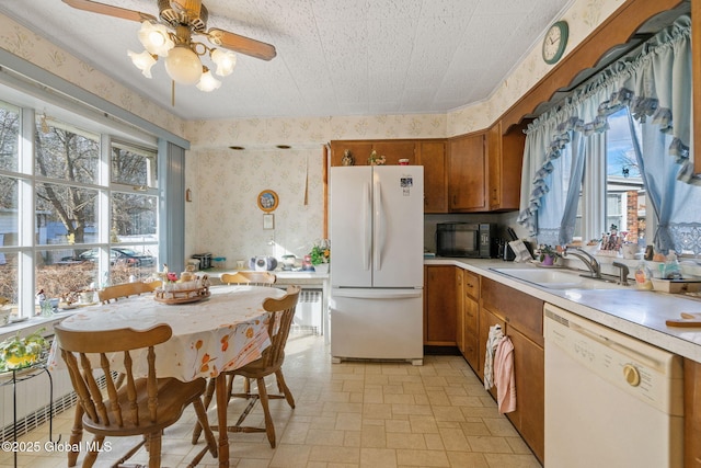 kitchen featuring a sink, wallpapered walls, white appliances, brown cabinetry, and light countertops