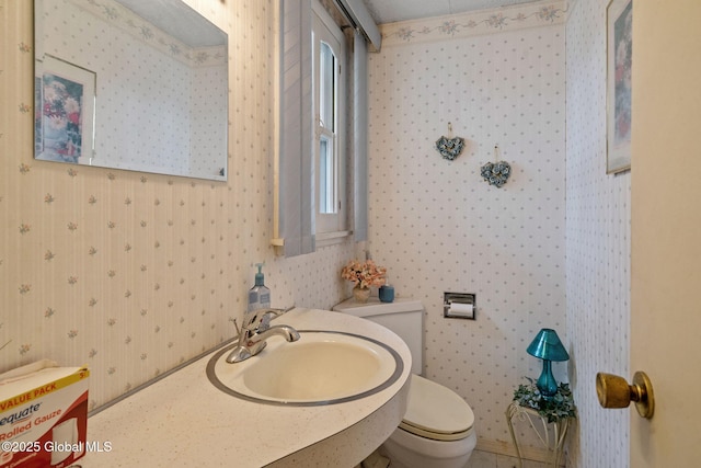 half bath featuring toilet, wallpapered walls, and a sink