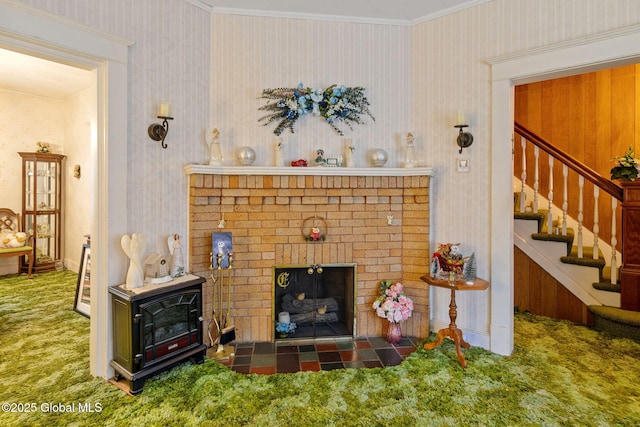 carpeted living room featuring crown molding, wallpapered walls, stairs, and a brick fireplace