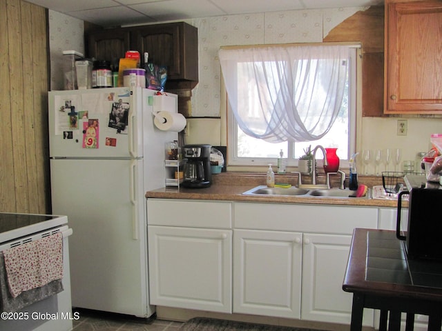 kitchen featuring a sink, white appliances, white cabinetry, and wallpapered walls