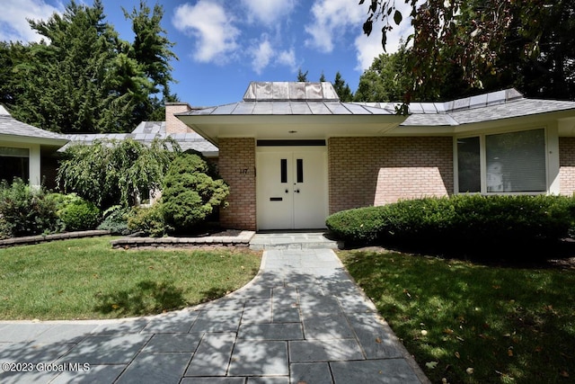 view of front facade featuring brick siding, a front yard, and a standing seam roof