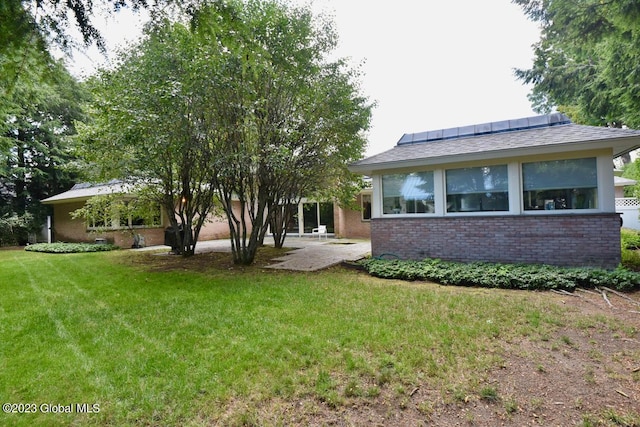 exterior space with solar panels, a patio, a lawn, and brick siding