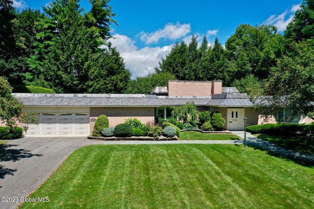 view of front of home with a front lawn, a standing seam roof, aphalt driveway, an attached garage, and brick siding