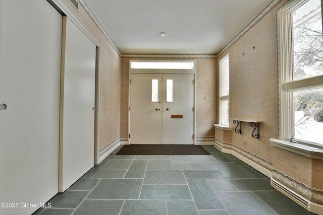 foyer entrance with crown molding, stone finish floor, and baseboards