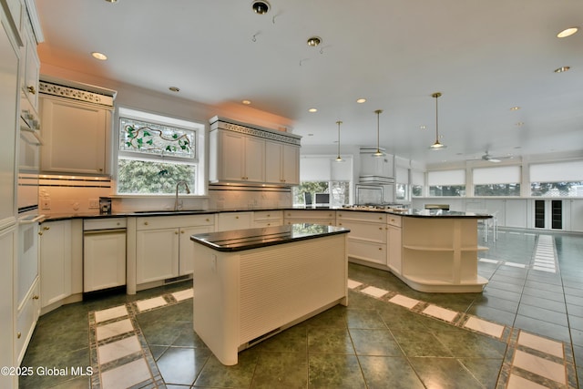 kitchen with a sink, decorative backsplash, dark countertops, and a peninsula