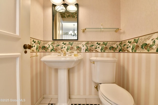 half bath with a chandelier, a wainscoted wall, toilet, and wallpapered walls