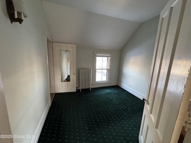 unfurnished room with vaulted ceiling, radiator heating unit, baseboards, and dark carpet