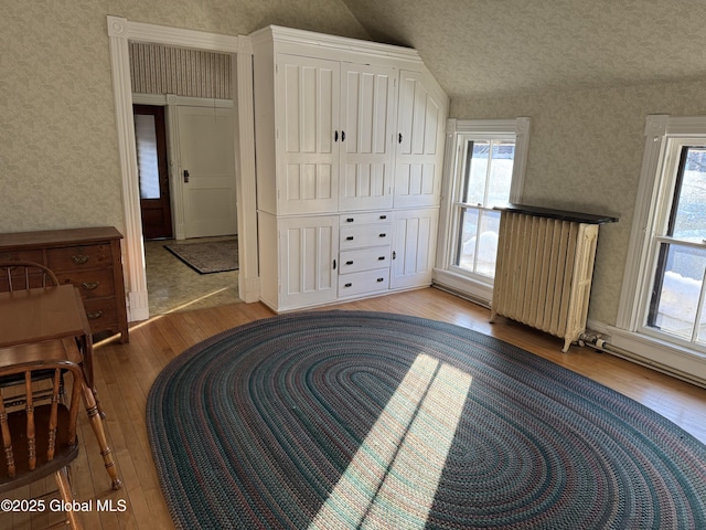 interior space featuring multiple windows, wallpapered walls, lofted ceiling, and hardwood / wood-style flooring