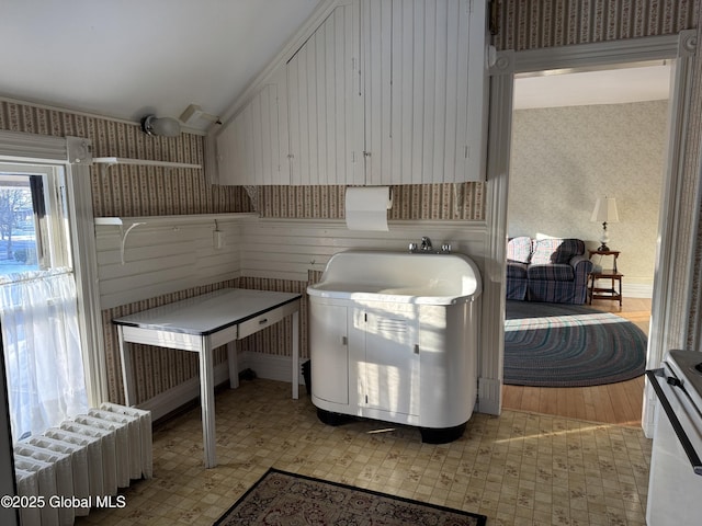 kitchen featuring radiator, wallpapered walls, electric range oven, vaulted ceiling, and white cabinetry