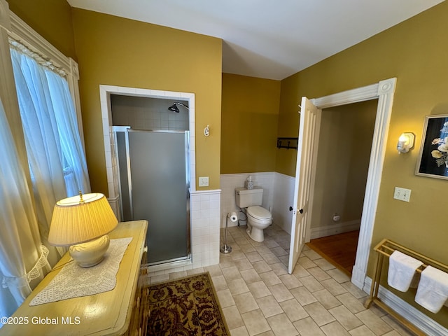 bathroom featuring toilet, wainscoting, a stall shower, tile patterned floors, and tile walls