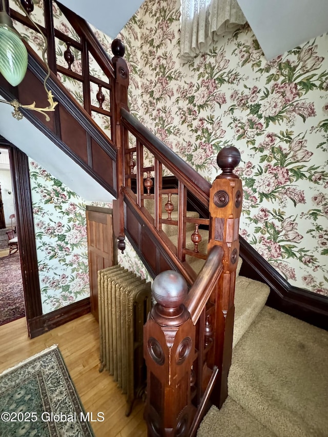 stairway featuring wallpapered walls, radiator heating unit, wood finished floors, and baseboards