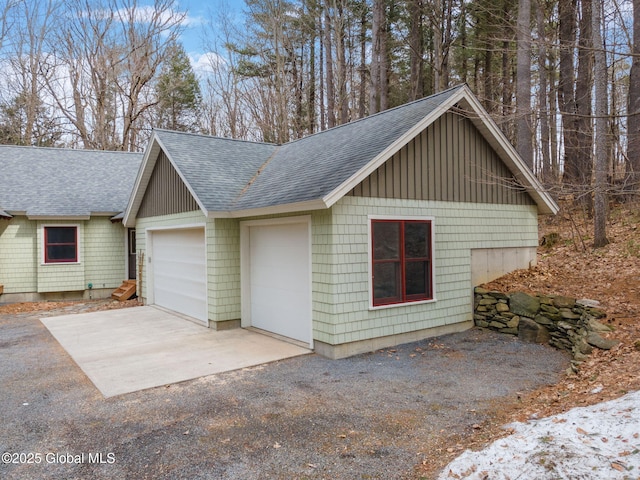 view of side of property with driveway, an attached garage, and roof with shingles