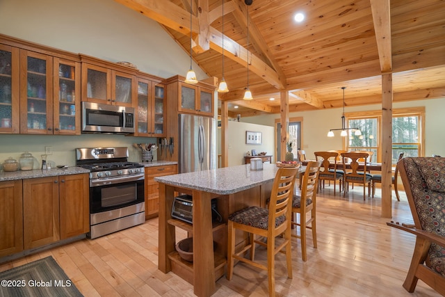 kitchen with beam ceiling, brown cabinets, stainless steel appliances, and light wood-type flooring