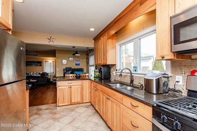 kitchen featuring a sink, tasteful backsplash, dark stone counters, appliances with stainless steel finishes, and a peninsula