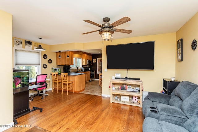 living area featuring baseboards, light wood-style flooring, and a ceiling fan