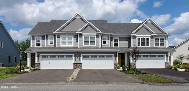 multi unit property featuring a garage, stone siding, driveway, and roof with shingles