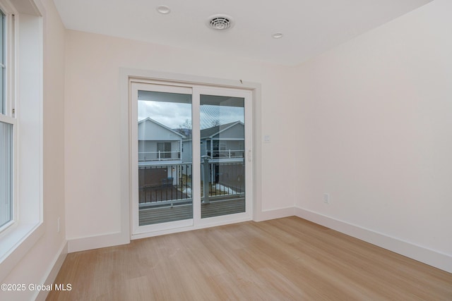 spare room featuring light wood-type flooring, visible vents, baseboards, and plenty of natural light