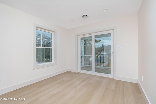 spare room with light wood finished floors, visible vents, and baseboards