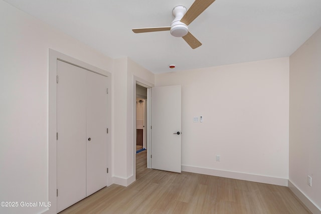 unfurnished bedroom featuring light wood finished floors, a closet, baseboards, and a ceiling fan