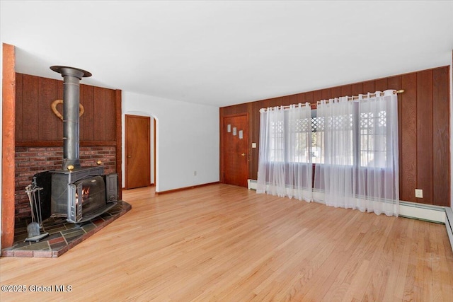 unfurnished living room with baseboards, wood walls, a wood stove, and light wood finished floors