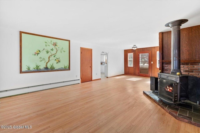 living area featuring a baseboard radiator, a wood stove, arched walkways, light wood-style floors, and wood walls