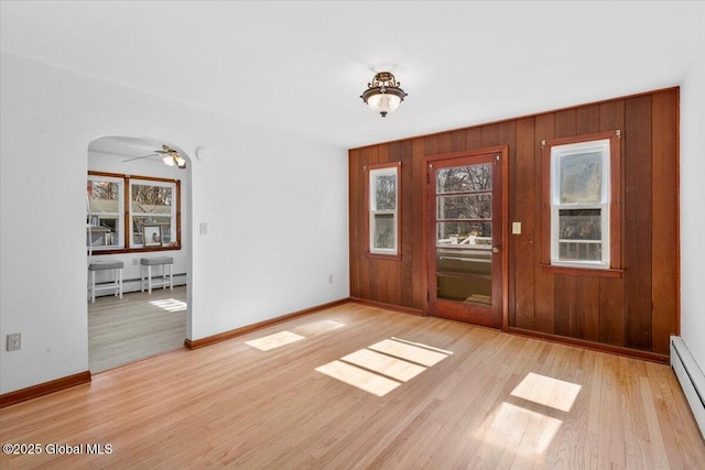 foyer featuring baseboards, baseboard heating, wood finished floors, arched walkways, and a baseboard radiator