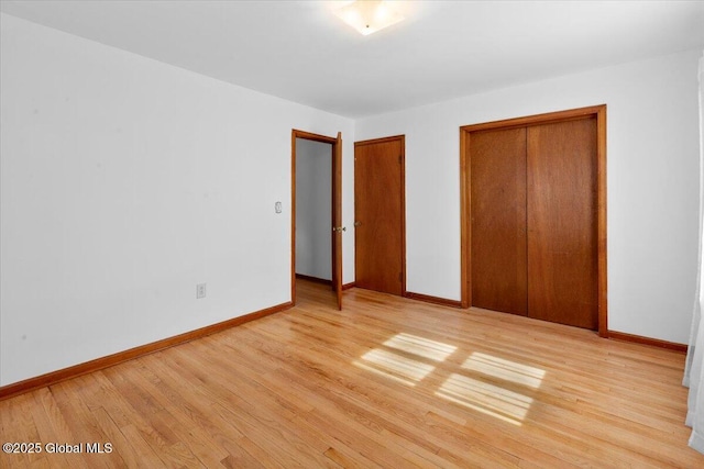 unfurnished bedroom featuring wood finished floors, baseboards, and multiple closets