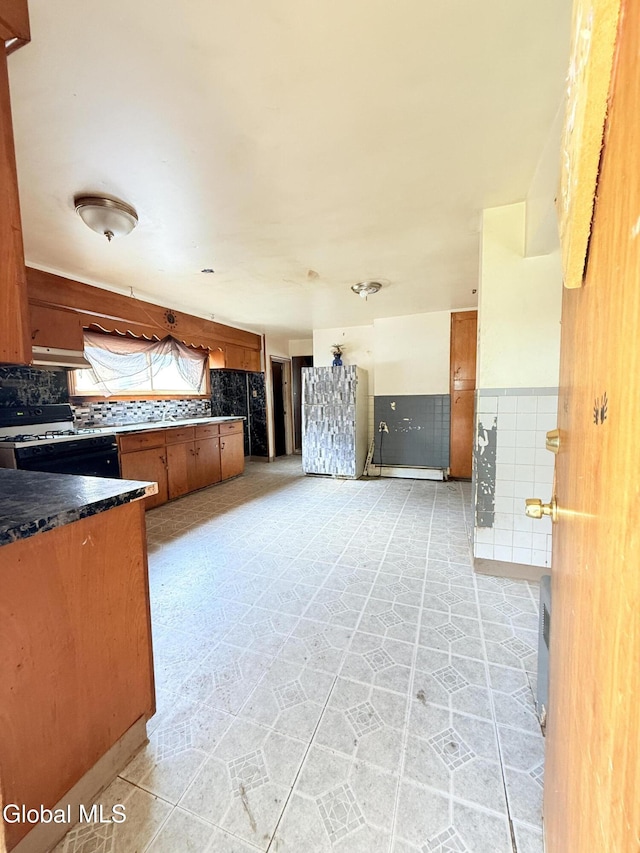3144 N Thompson St, Rotterdam, NY 12306 - kitchen with under cabinet range hood, dark countertops, brown cabinets, range with gas stovetop, and backsplash