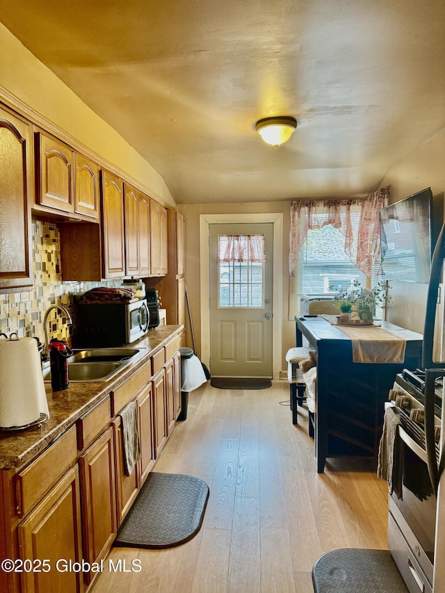 kitchen featuring a sink, brown cabinets, light wood-style floors, and dark countertops