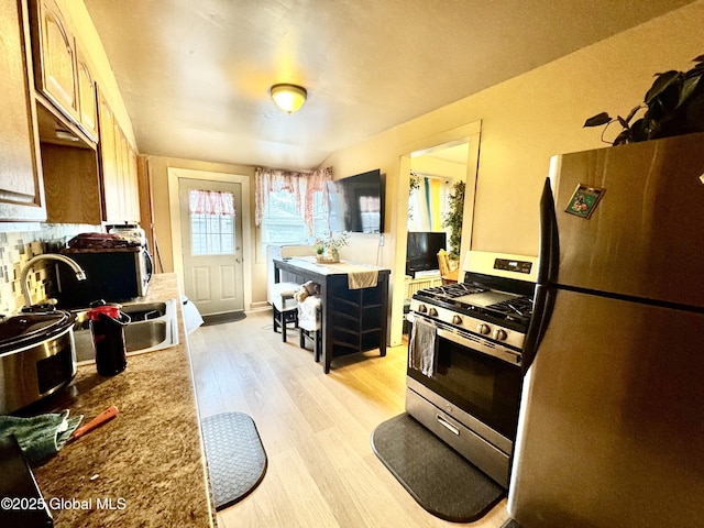 kitchen with light wood-style flooring, a sink, backsplash, appliances with stainless steel finishes, and light countertops