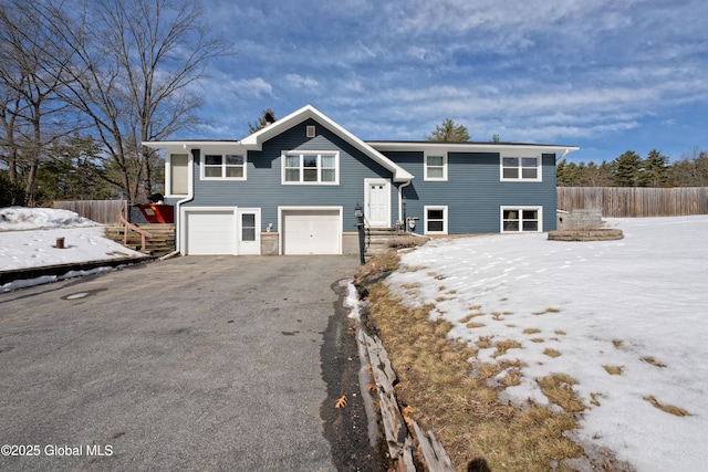 raised ranch featuring aphalt driveway, an attached garage, and fence