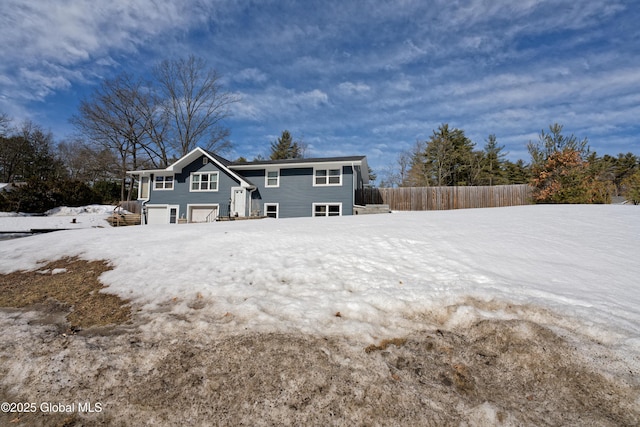 snow covered back of property with an attached garage and fence