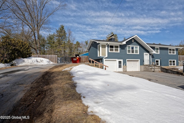 raised ranch with a garage, stone siding, driveway, and fence